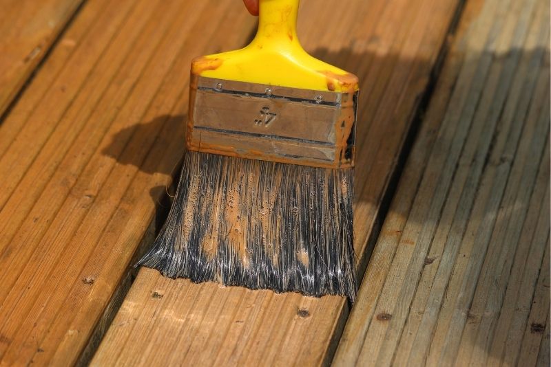 A paintbrush applying wood stain to timber decking boards