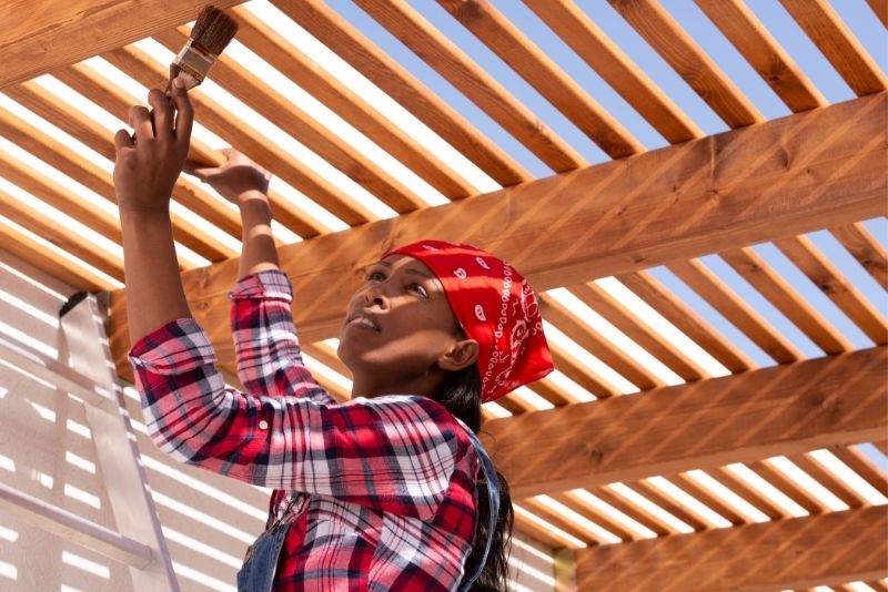 Woman staining the timber beams of a pergola structure